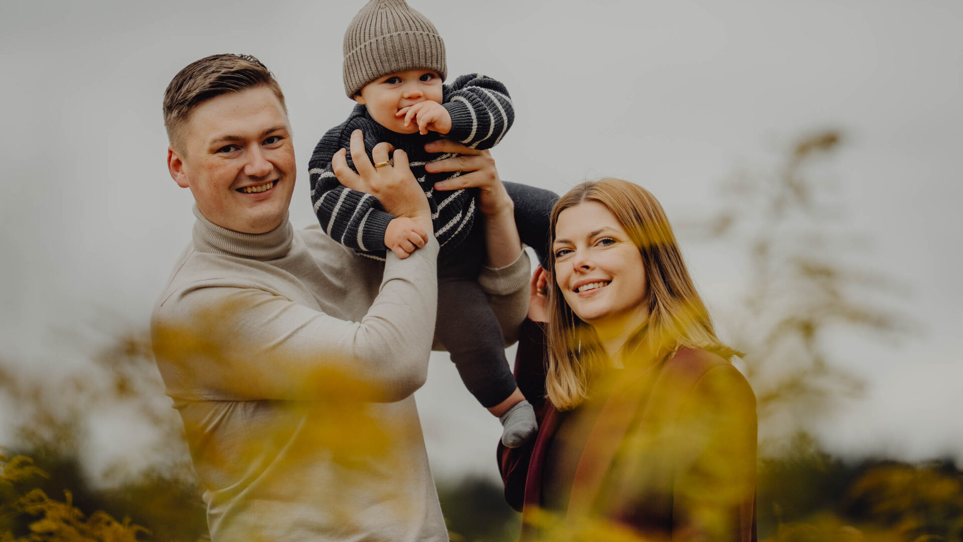Rodzice podnoszą do góry dziecko na sesji na łące w Supraślu.