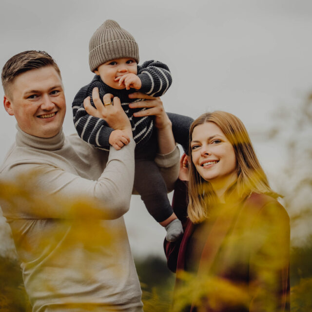 Rodzice podnoszą do góry dziecko na sesji na łące w Supraślu.