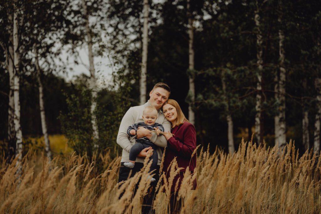 Rodzice przytulają dziecko na sesji na łące wśród traw.