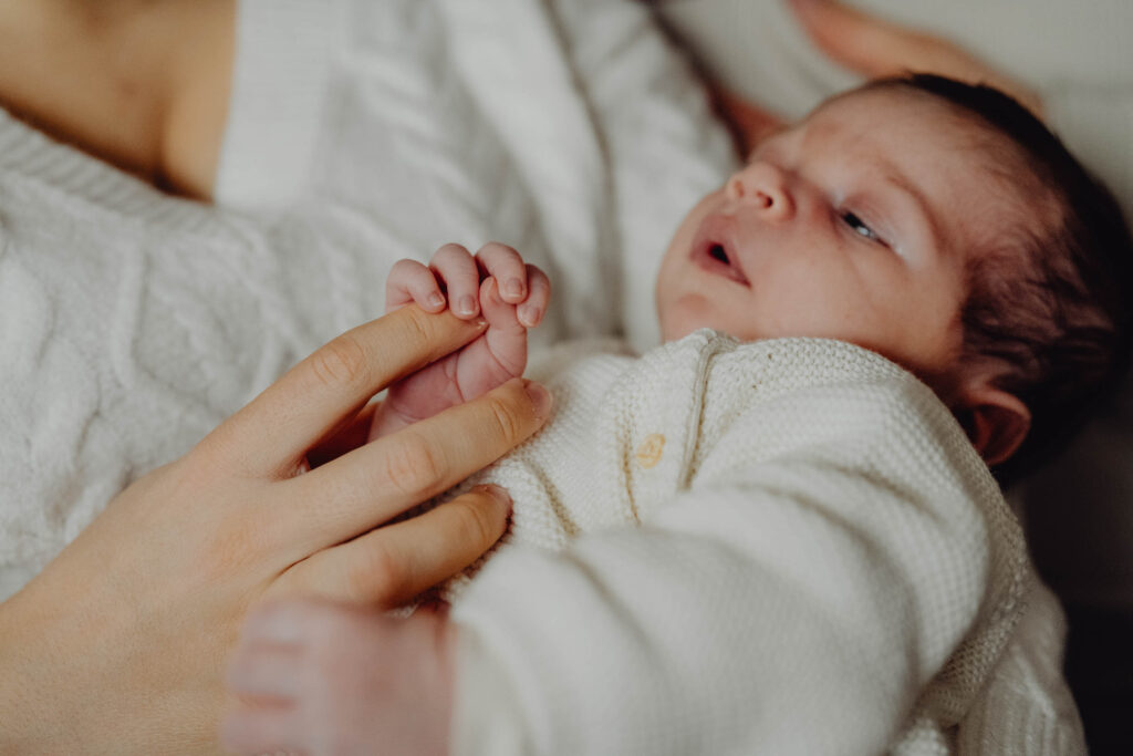 Fotografia malutkiej dłoni noworodka ściskającego palec swojej matki.