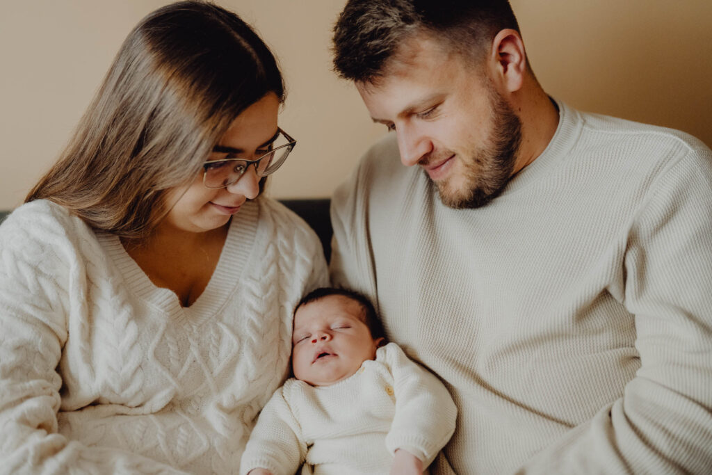 Rodzice tulą swoje dziecko siedząc na kanape w swoim domu.