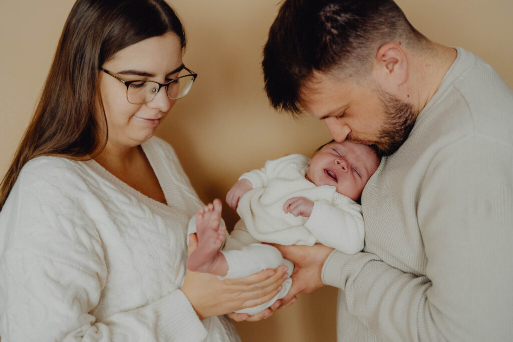 Ojciec całuje swoje 2 tygodniowe dziecko w główkę.