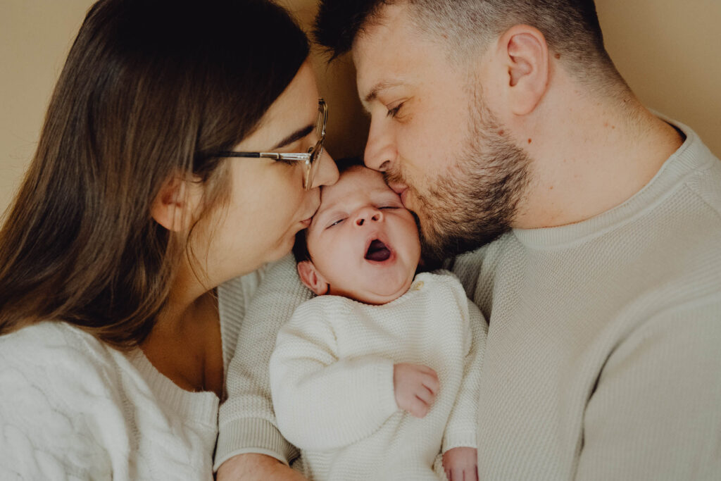 Rodzice całują swoje 2 tygodniowe dziecko w czółko a ono ziewa.