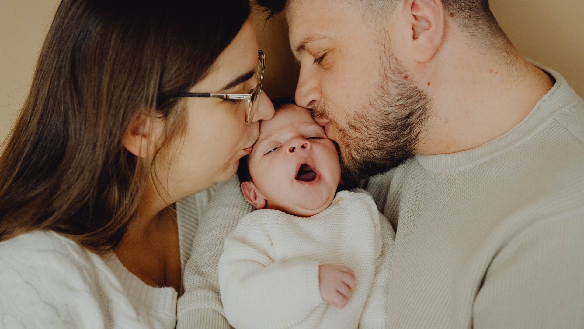 Rodzice całują swoje 2 tygodniowe dziecko w czółko a ono ziewa.