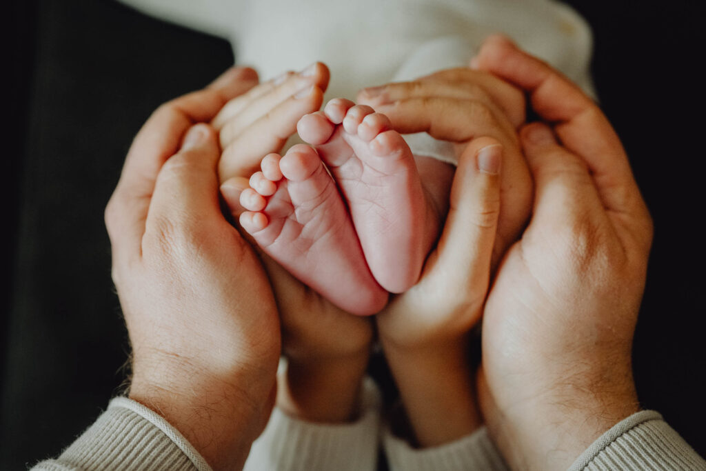 Małe bose stópki noworodka oplecione w dłoniach jego rodziców.