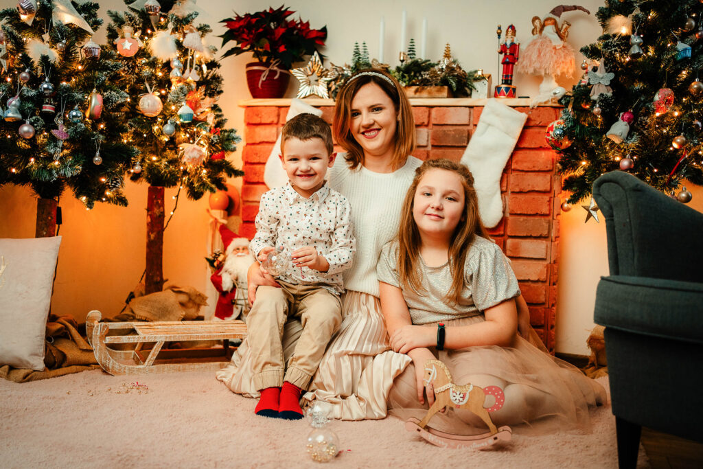 Mama siedzi ze swoimi dziećmi przed komikiem na rodzinnej sesji świątecznej w domu.