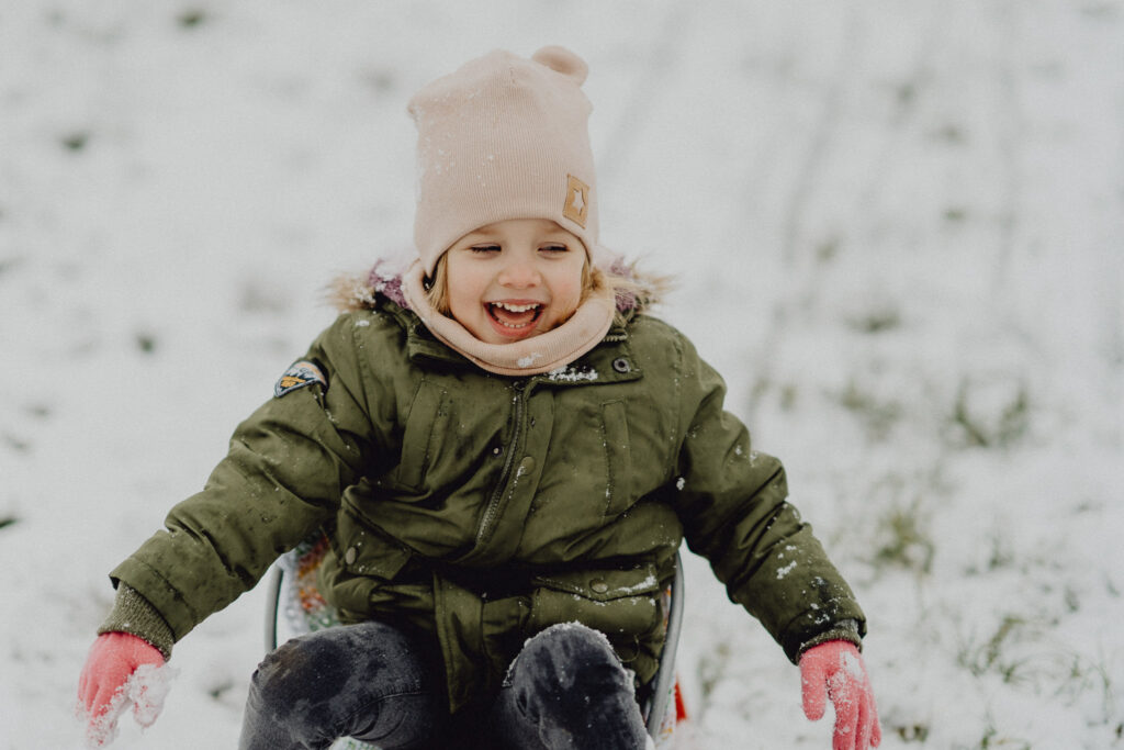 Uśmiechnięta od ucha do ucha dziewczynka jest ciągnięta na sankach podczas sesji lifestyle w Białymstoku.